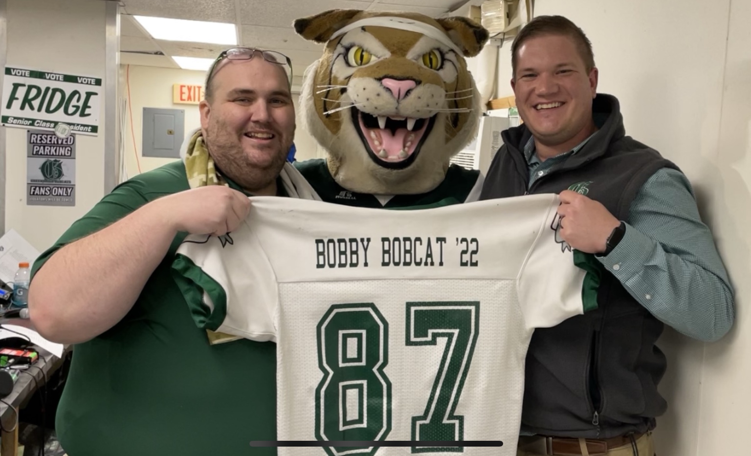 Bobby and two adults holding a jersey marked Bobby Bobcat ’22.